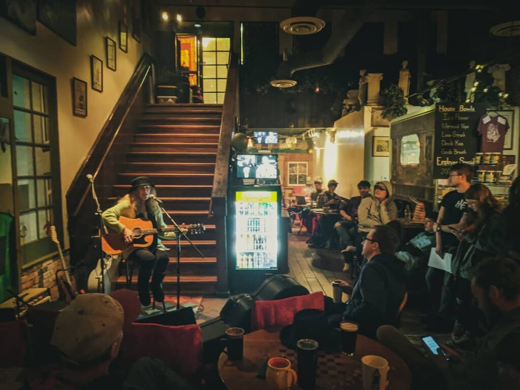 A woman performs a song with a guitar in front of a crowd in the Espresso Art Cafe.